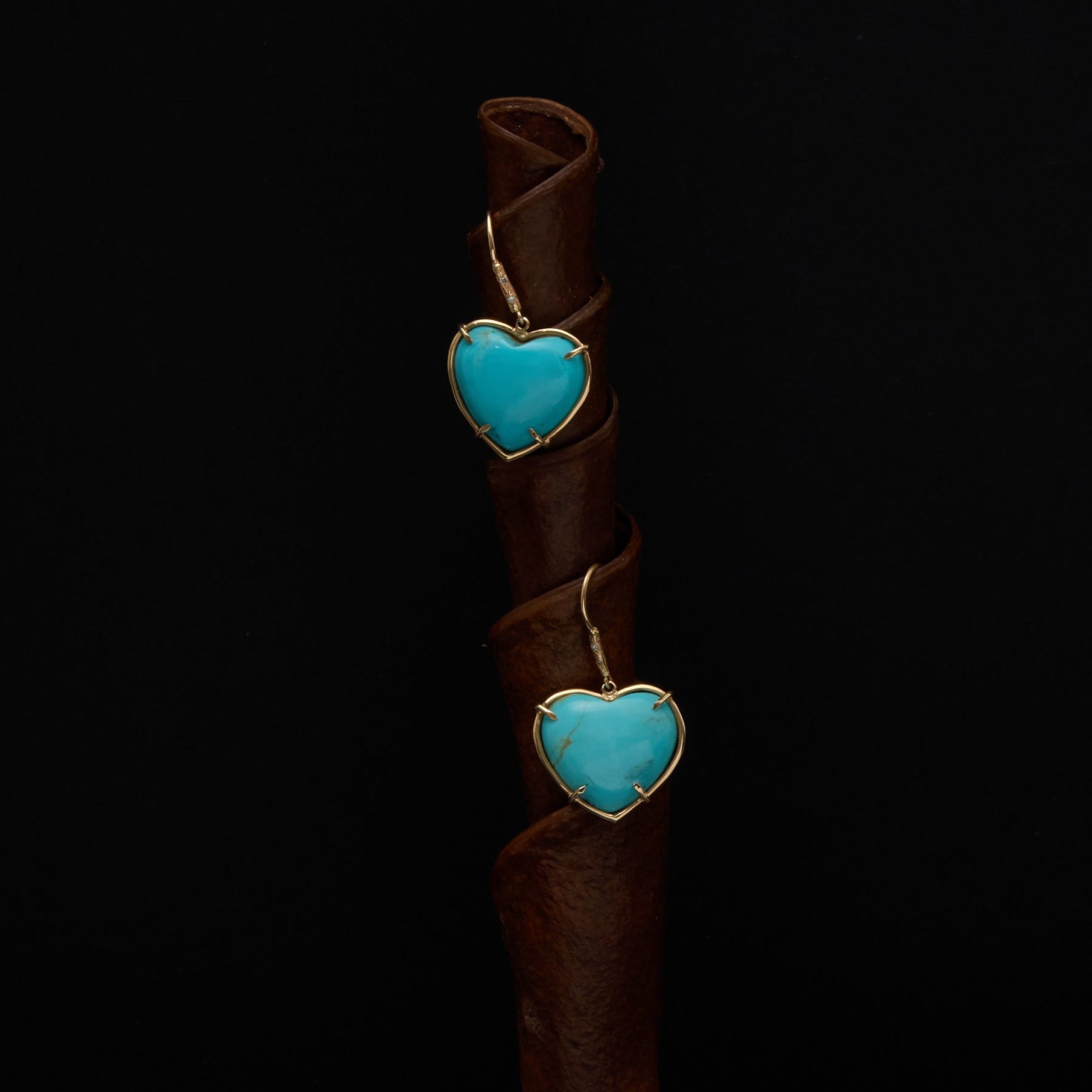 A brown leather spiral phone stand with two turquoise heart charms, shown on a dark surface.