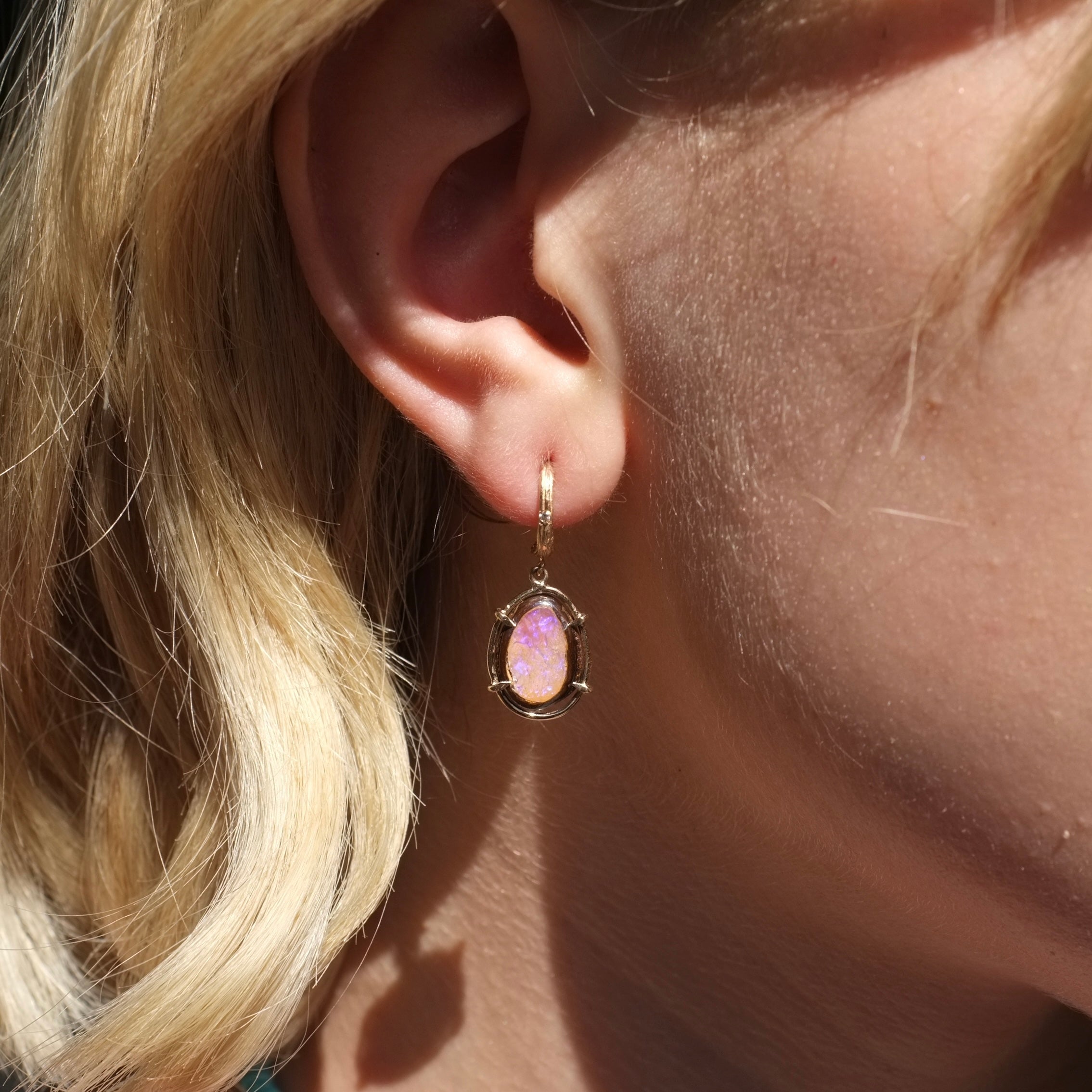 Close-up of an ear wearing a pink opal earring with blonde hair.