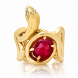 A gold snake ring with a large oval red ruby center stone and small diamond eyes, shown on a white background with a soft reflection.