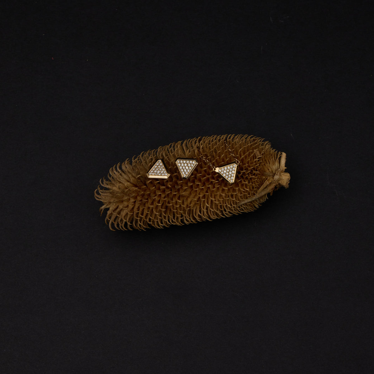 A small brown textured accessory with three small triangular gold-tone studs set with clear stones, photographed on a solid black background.