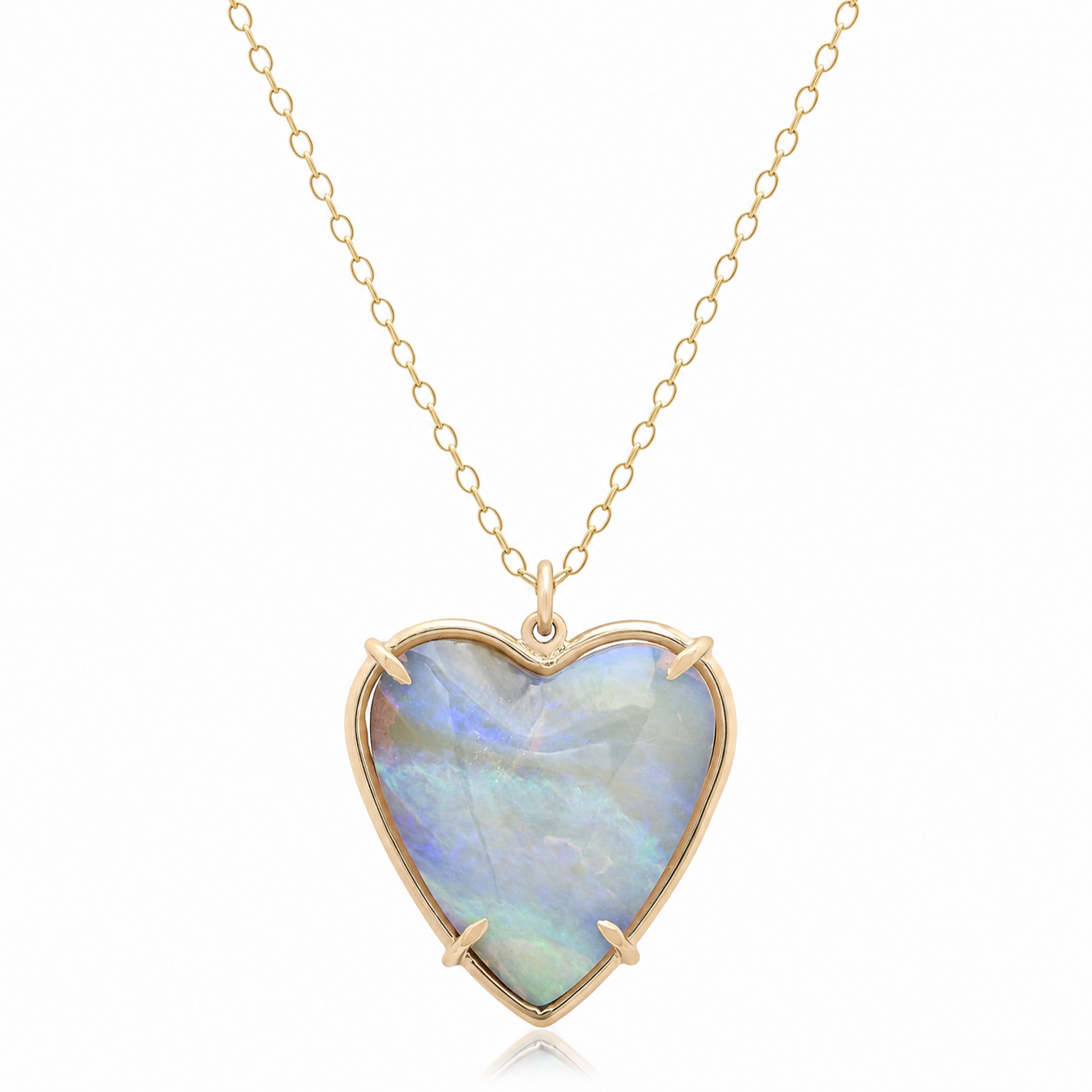 A heart-shaped pendant necklace featuring a milky white opal with blue and green iridescence, set in a gold bezel and suspended from a delicate gold chain against a white background.