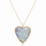 A heart-shaped pendant necklace featuring a milky white opal with blue and green iridescence, set in a gold bezel and suspended from a delicate gold chain against a white background.